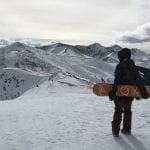 Stephanie Kemp on top of Peak 6 holding a snowboard