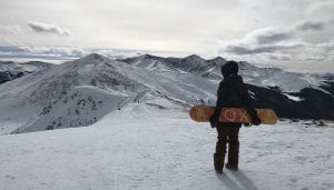 Stephanie Kemp on top of Peak 6 holding a snowboard