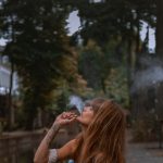 woman smoking near green trees during daytime