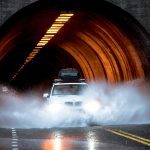 white BMW car crossing asphalt road in front of concrete tunnel